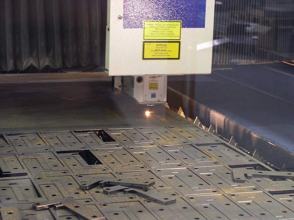 Głowica wycinarki laserowej nad arkuszem z wyciętymi detalami
